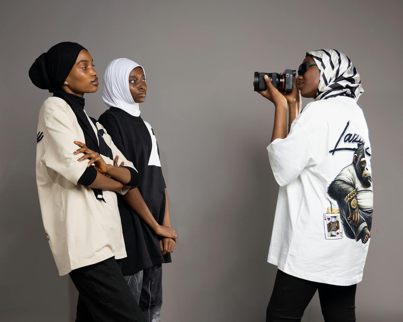 Three women in stylish clothing engaged in a studio photo shoot, showcasing modern fashion.