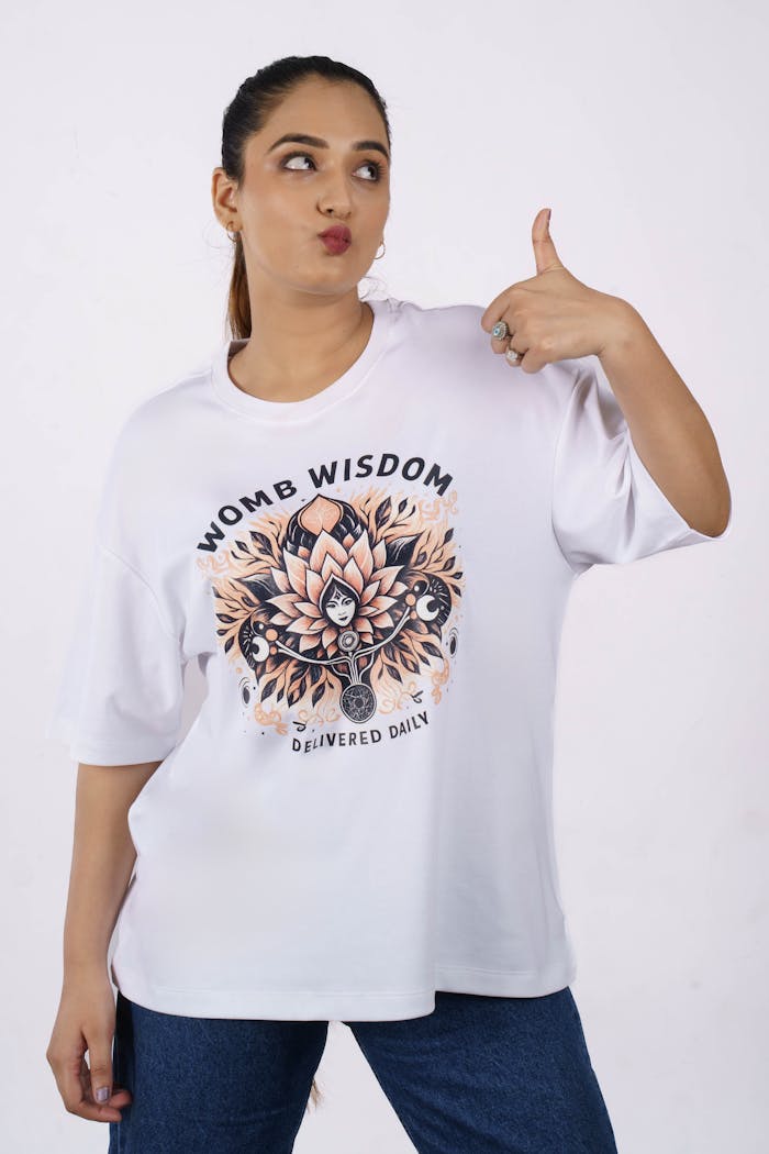 Person in white oversized T-shirt featuring 'Womb Wisdom' graphic. Casual fashion style.